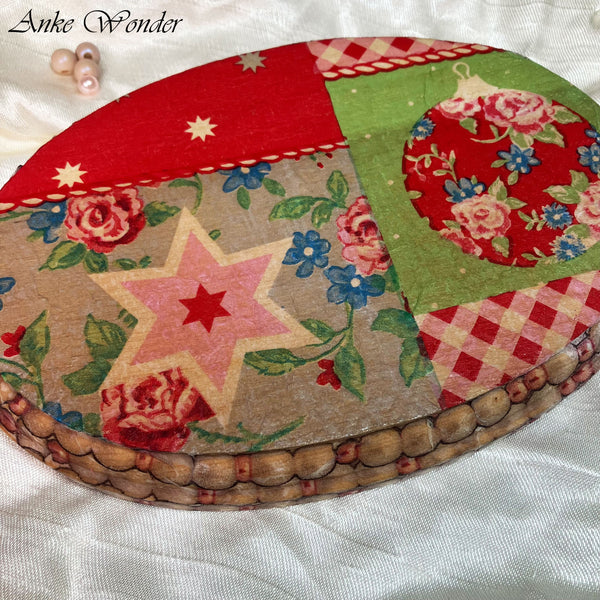 A detailed close-up of a handmade wooden wall decor featuring a vintage-inspired Christmas design. The intricate decoupage showcases a floral ornament, a pink star motif, and festive patchwork in red, green, and beige tones. The texture of the wood and the eco-friendly sealant give it a rustic, handcrafted finish, with a handwoven edge adding an artisanal touch.