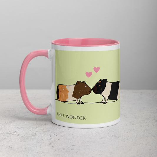 Left side of green ceramic mug showing two adorable guinea pigs and the Anke Wonder logo, with a vibrant pink handle.