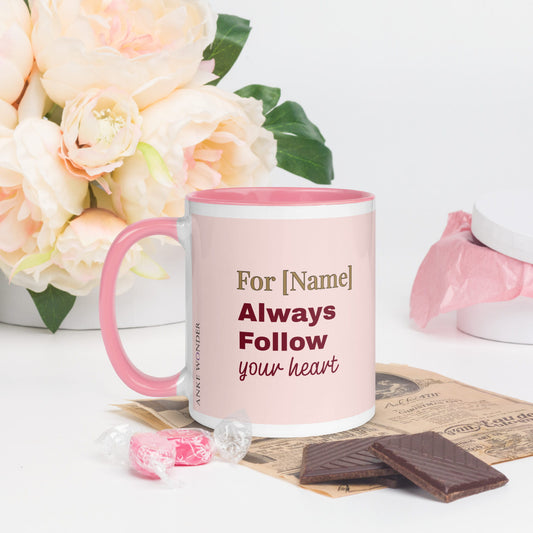 Personalized mug with pink handle and text, surrounded by flowers and chocolates on a light background
