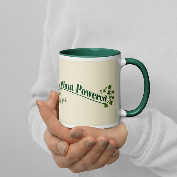 Right view of a ceramic mug with the phrase 'Plant Powered' in green, featuring a green handle and rim, held by a person wearing a white sweater.