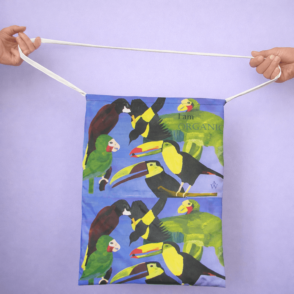 Bag with colorful parrot illustrations held by two hands against a light purple background