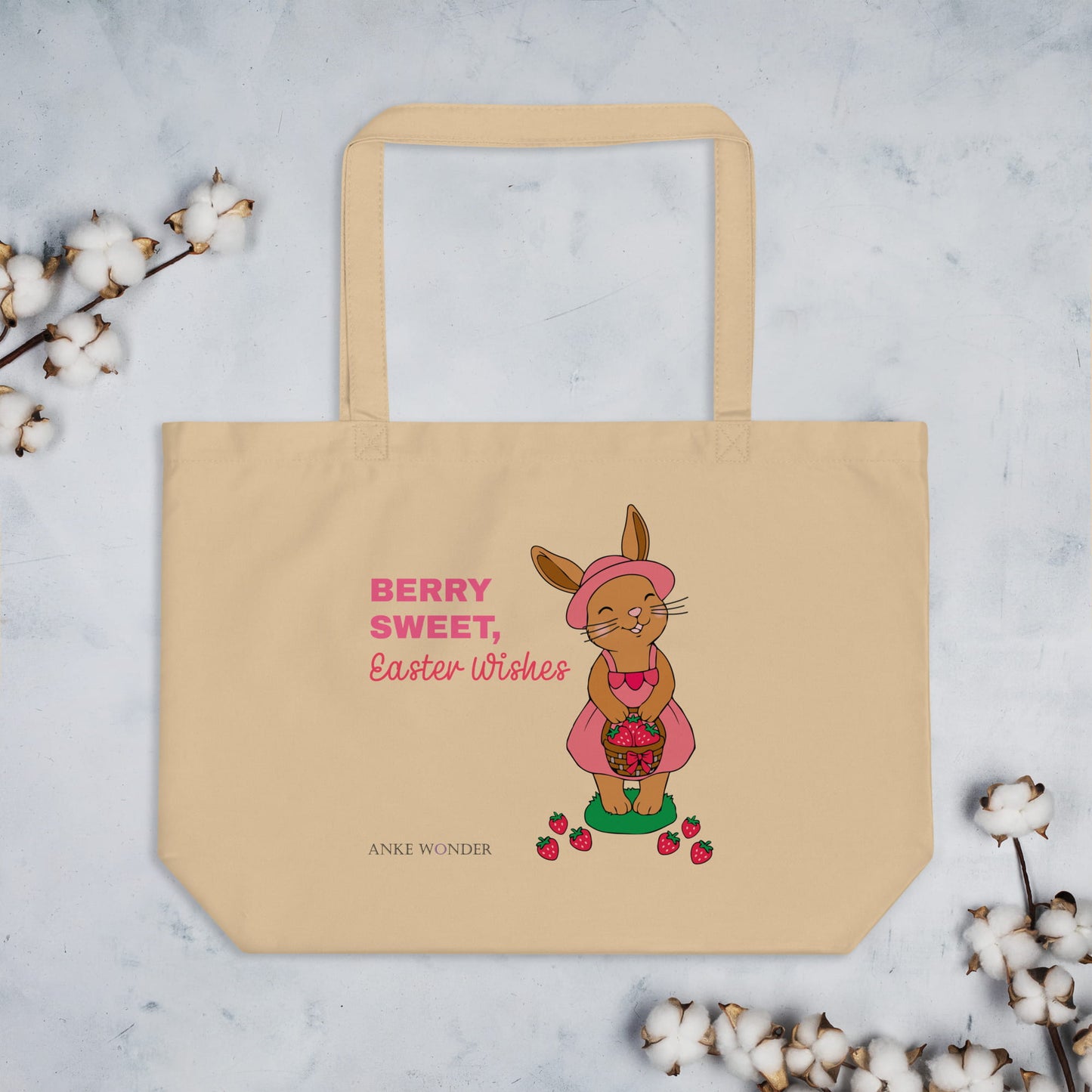 Beige tote bag with Easter-themed design featuring a rabbit with strawberry basket and text 'Berry Sweet Easter Wishes', surrounded by cotton branches on a light background.