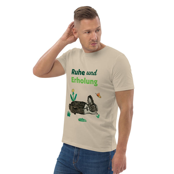 Man wearing desert dust organic cotton t-shirt at right angle, showing "Ruhe & Erholung" text and hand-painted rabbit, butterfly, and foliage design.