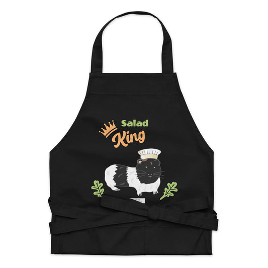 A detailed flat-lay of the black apron, highlighting the adorable guinea pig chef design and playful text.