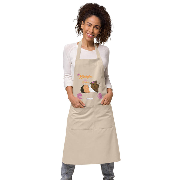 A woman wears a natural-colored apron featuring a guinea pig with a pink crown and the text “Königin der Küche.