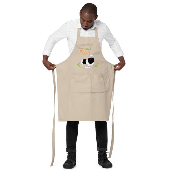 Man models wearing a beige Salad King apron, showcasing a guinea pig in a chef hat and decorative lettuce illustrations with adjustable strings.