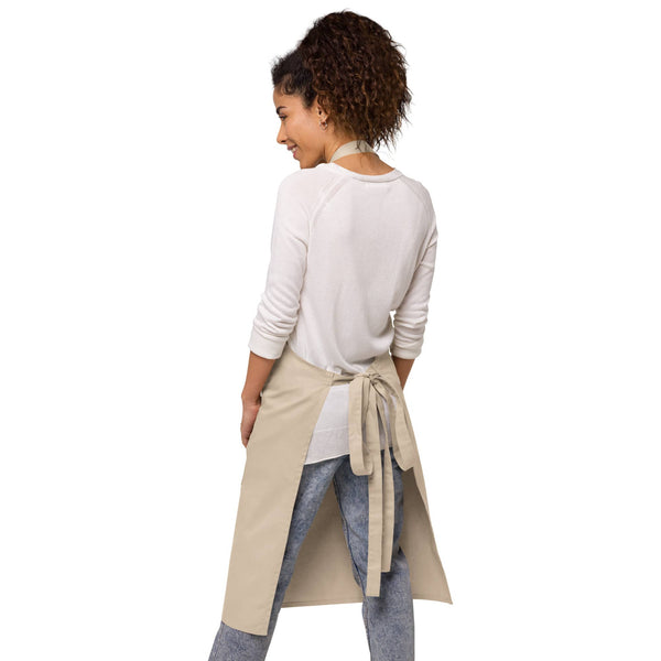 A woman is seen from behind, wearing the natural beige apron with adjustable straps and a tied waist.