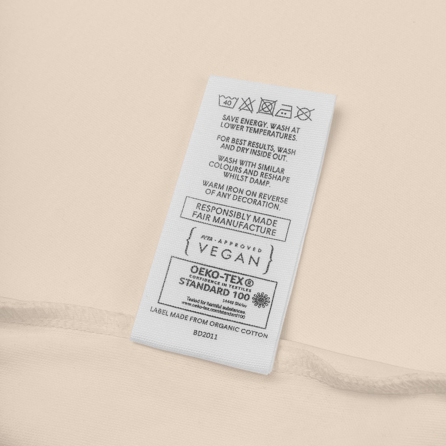 Close-up of organic cotton, peta-approved vegan label of beige baby onesie by Anke Wonder.