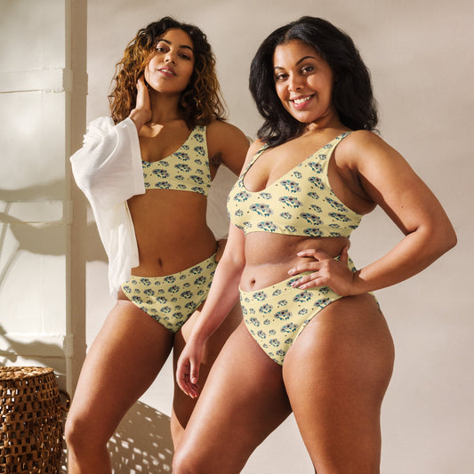 Two women wearing a matching yellow floral bikini set with sunflowers and bees against a neutral background.