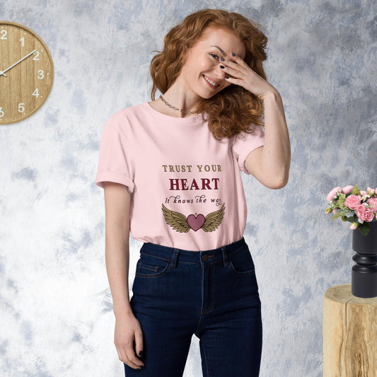 Woman wearing a pink t-shirt with a motivational quote and design, standing against a gray textured wall.