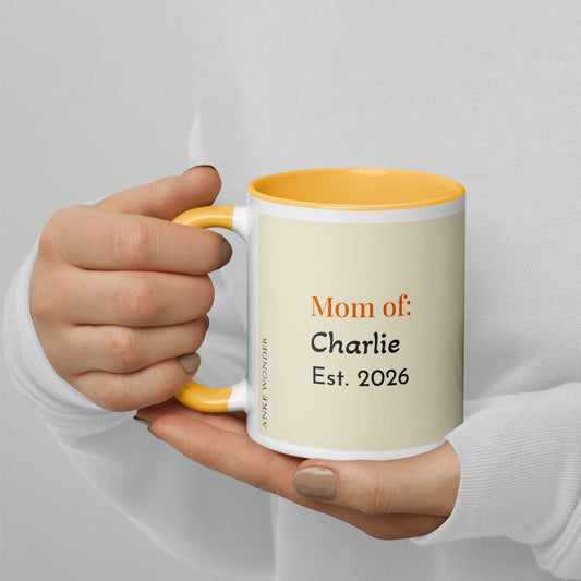 Hand holding a mug with text 'Mom of: Charlie Est. 2026' against a light gray background