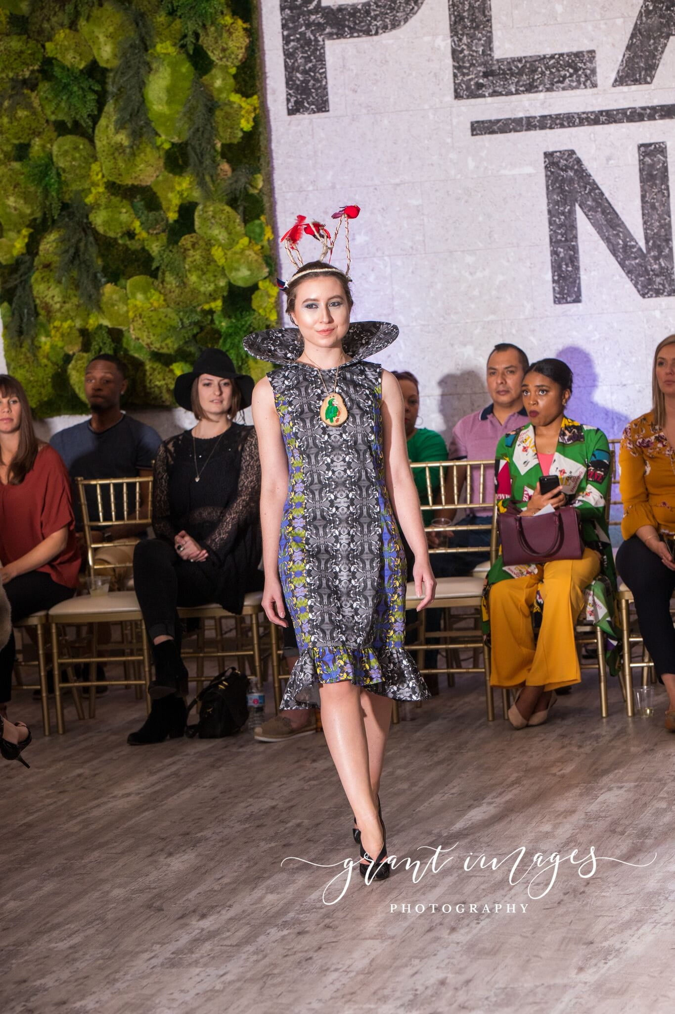 Model walking on a runway at a fashion event with fake, red birds in her hair.