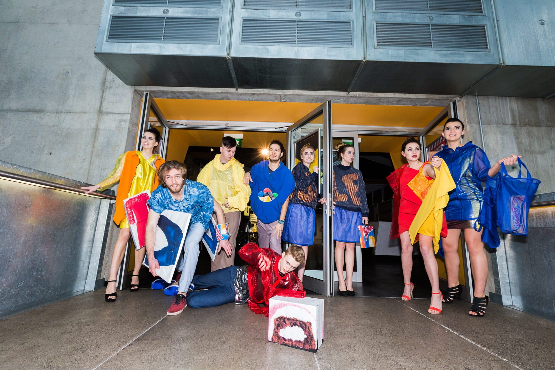 Group of people in colorful outfits standing in front of a modern building entrance.