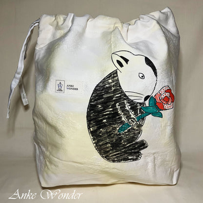 White drawstring bag with a black and white illustration of a rabbit holding a red flower, on a beige background.