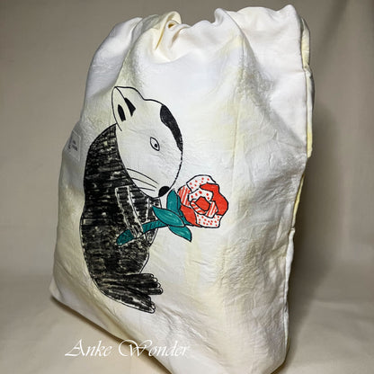 White drawstring bag with a black and white rabbit holding a red rose design on a beige background.