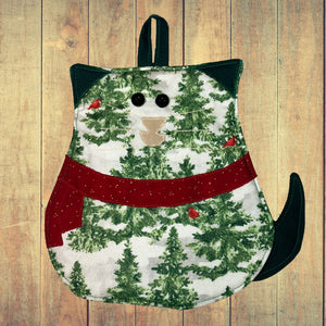 Front view of a festive cat-shaped potholder with a holiday design featuring green pine trees, red cardinals, and a red scarf. The potholder has black button eyes and a tan nose, creating a charming cat face on the front.