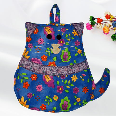 Front view of a cat-shaped potholder with a charming blue floral design, featuring purple ears and a matching purple fabric necklace. The potholder has black button eyes and a small tan nose, creating an adorable cat face perfect for adding a touch of whimsy to the kitchen.