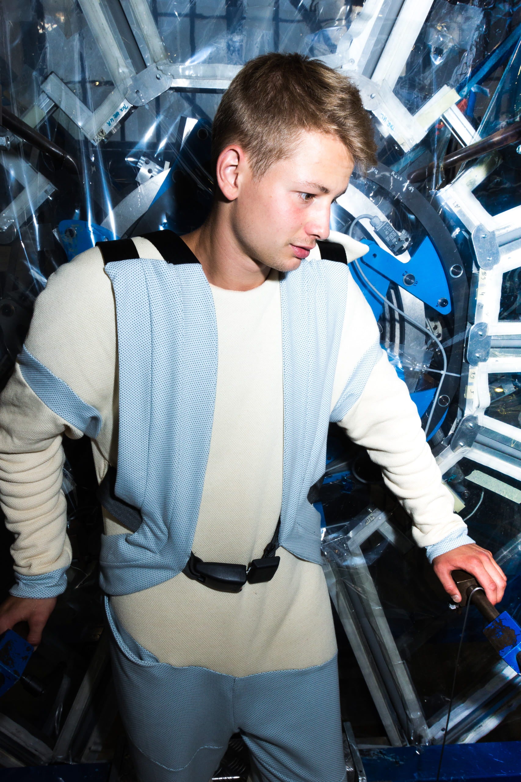 Men standing in a machine, wearing a blue overall outfit.