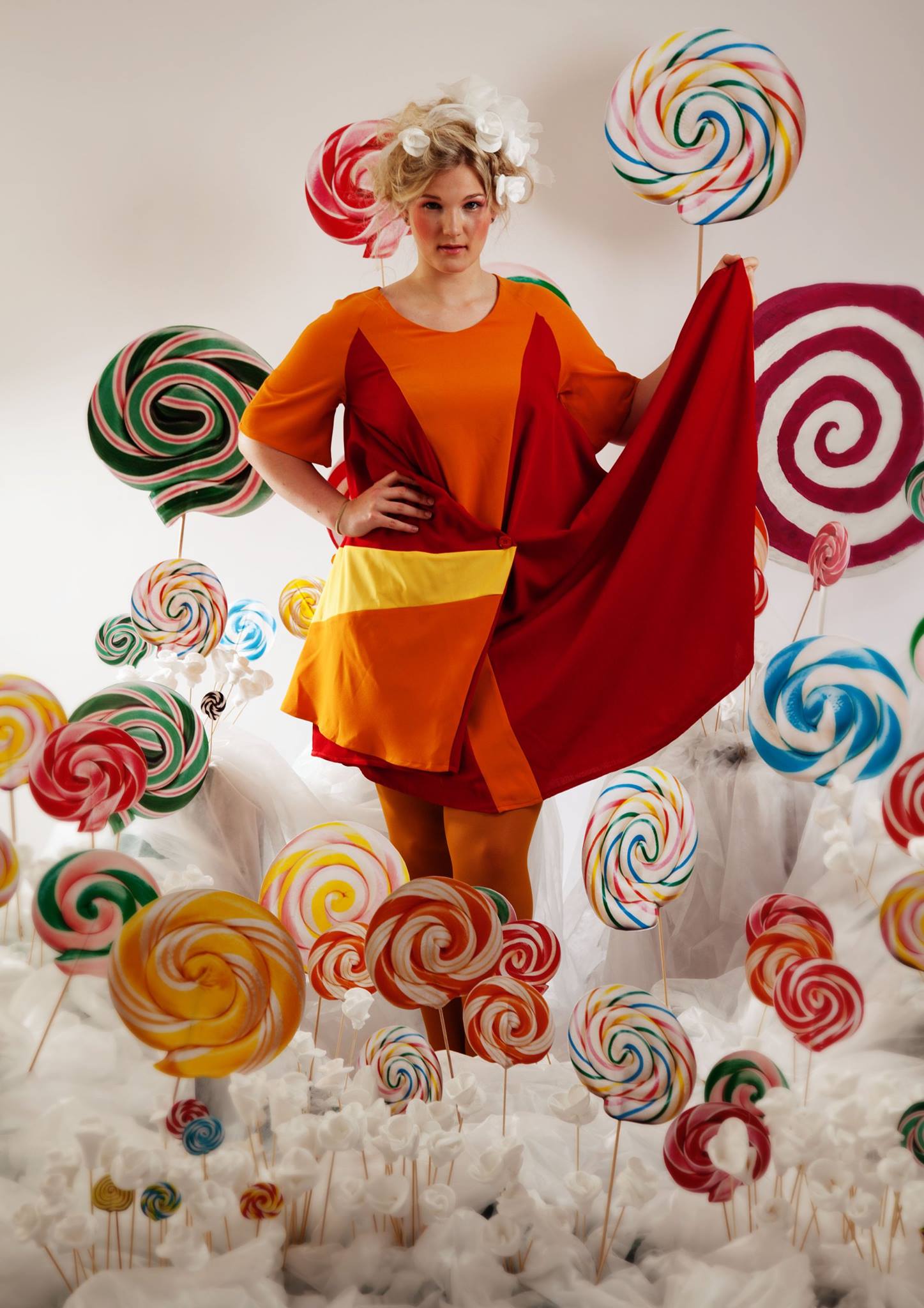 Woman in a colorful dress surrounded by oversized lollipops against a white background