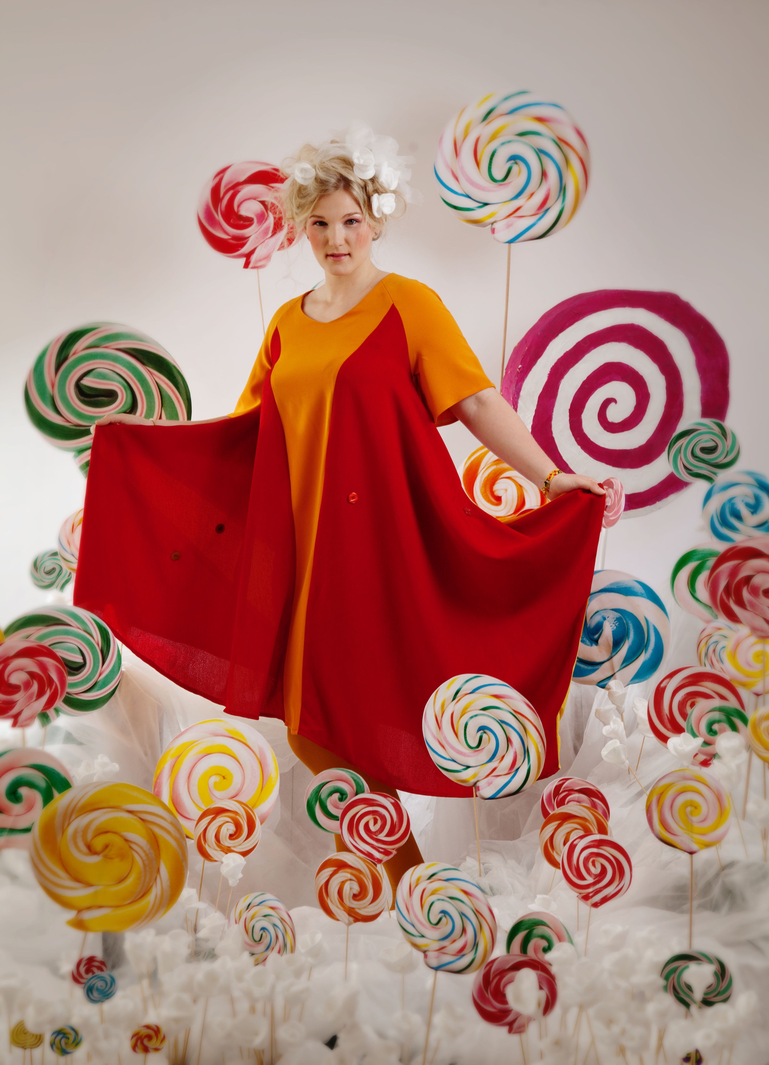Person wearing a colorful dress surrounded by oversized lollipop decorations on a white background