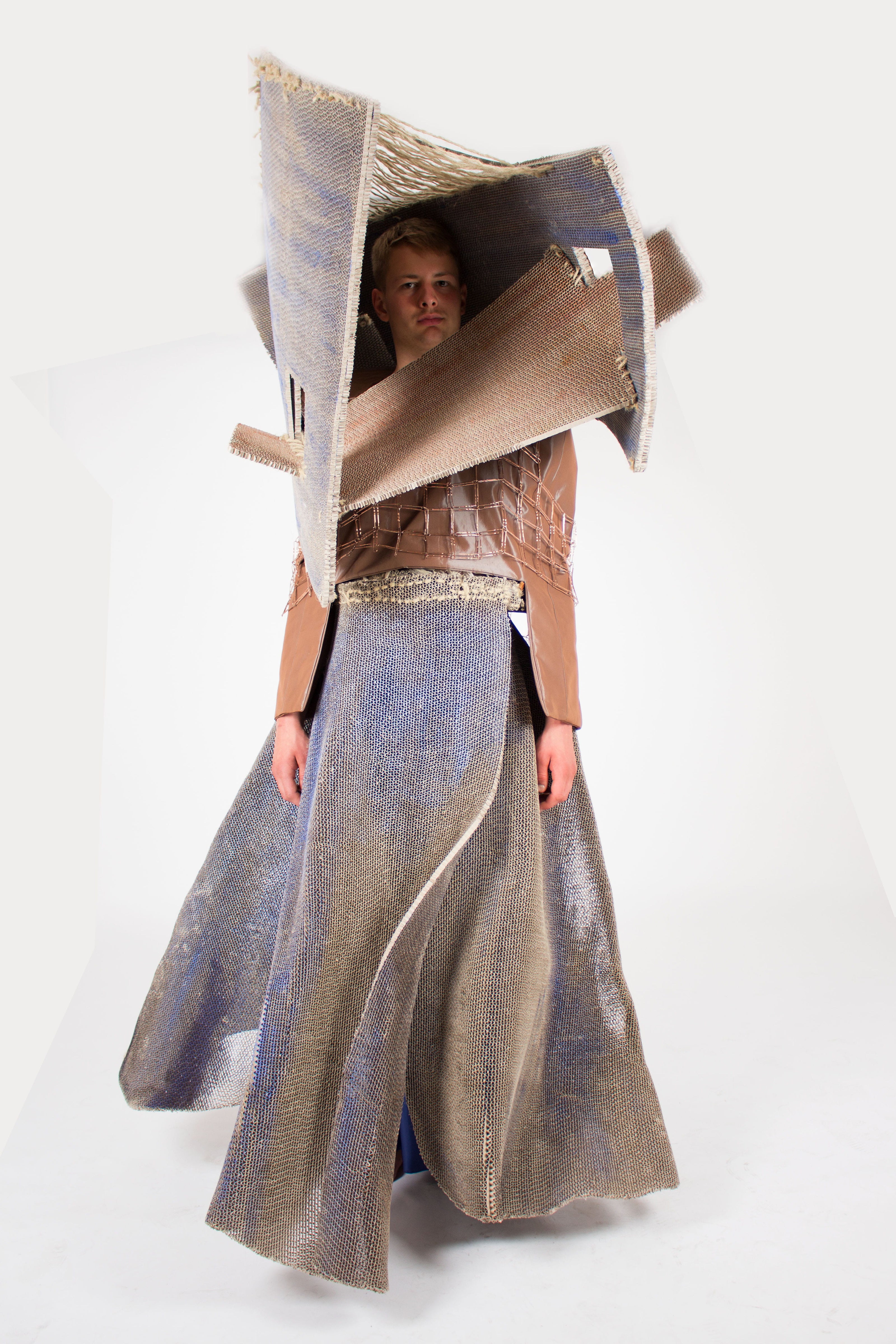 Person wearing a metallic dress with a large book-like object on their head against a white background