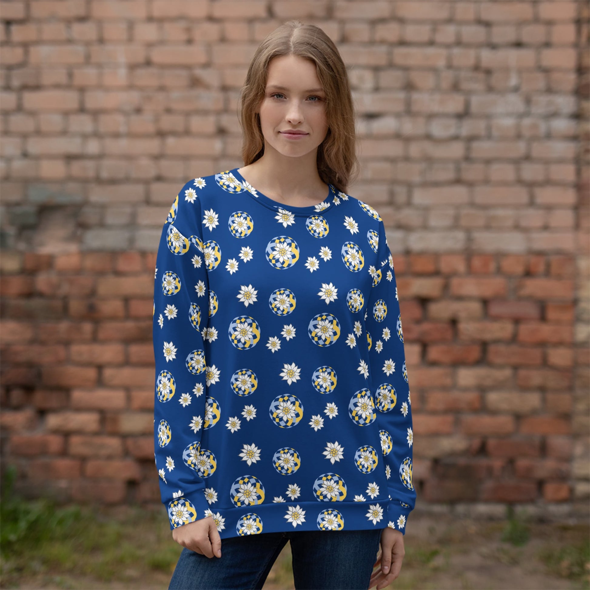 Woman wearing a blue floral patterned sweater with Edelweiss pattern standing in front of a brick wall.