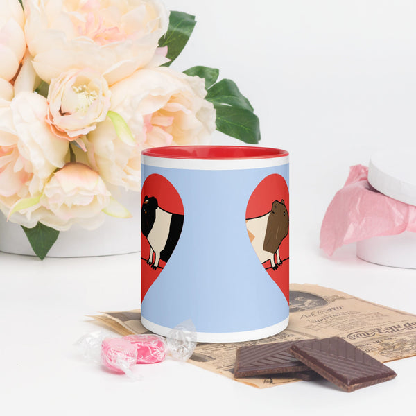 Front view of blue ceramic mug featuring two cute guinea pigs nestled in a red heart, with red accents on the rim and handle.