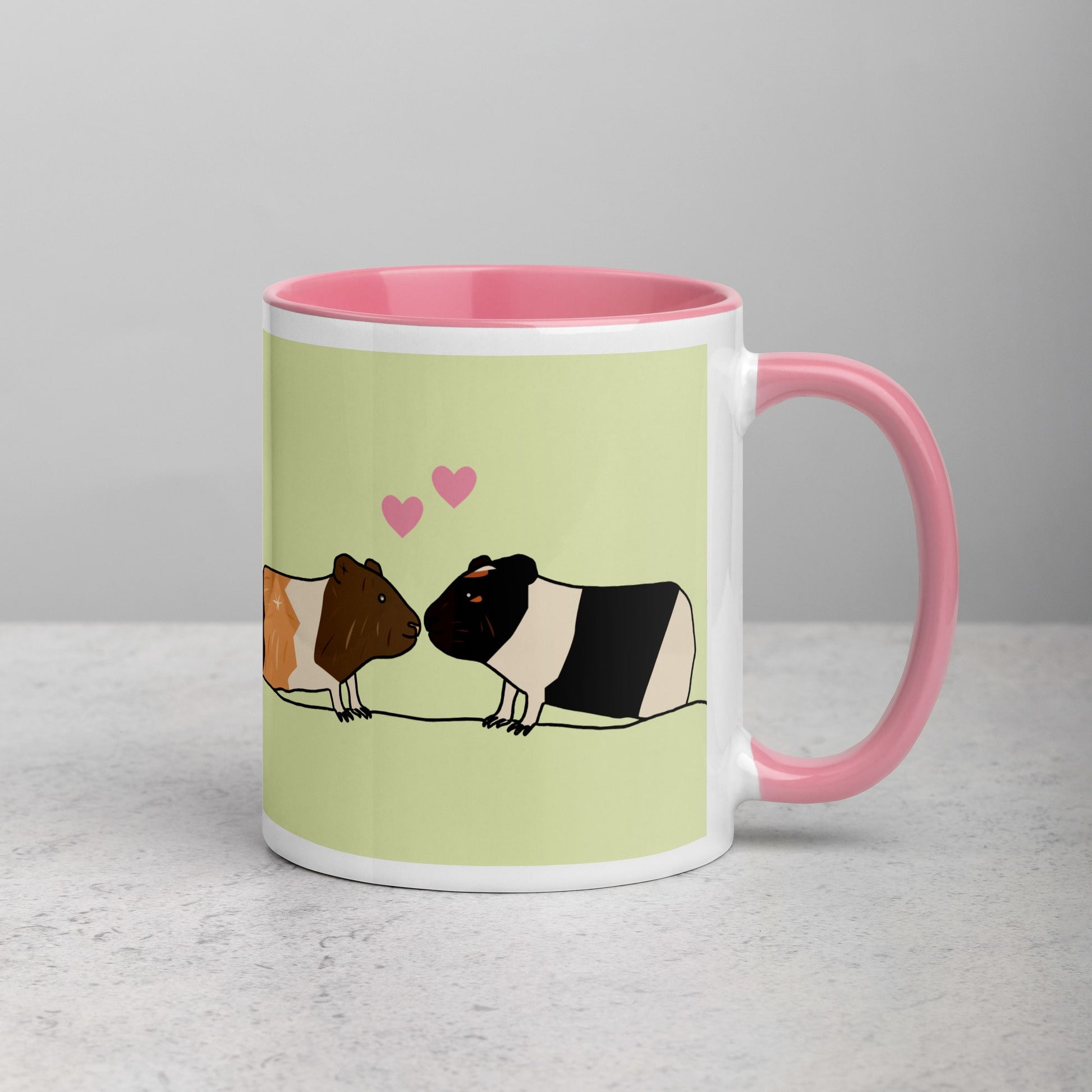 Right side view of green ceramic mug featuring two guinea pigs, one black and white and one brown and white, with a playful pink handle.