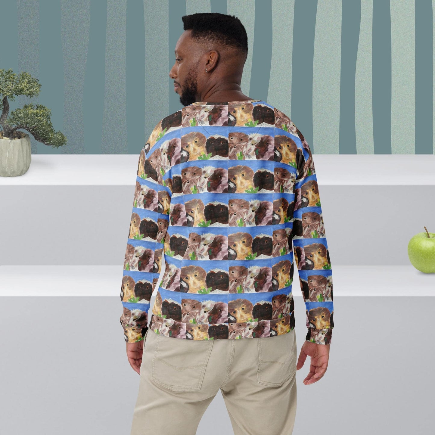 Man wearing a long-sleeve shirt with guinea pig pattern in a room with striped wallpaper.