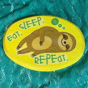 Hand-painted wooden wall decor featuring a sleeping sloth with the words "Eat, Sleep, Repeat" on a bright yellow background.