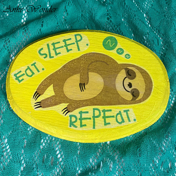 Hand-painted wooden wall decor featuring a sleeping sloth with the words "Eat, Sleep, Repeat" on a bright yellow background.