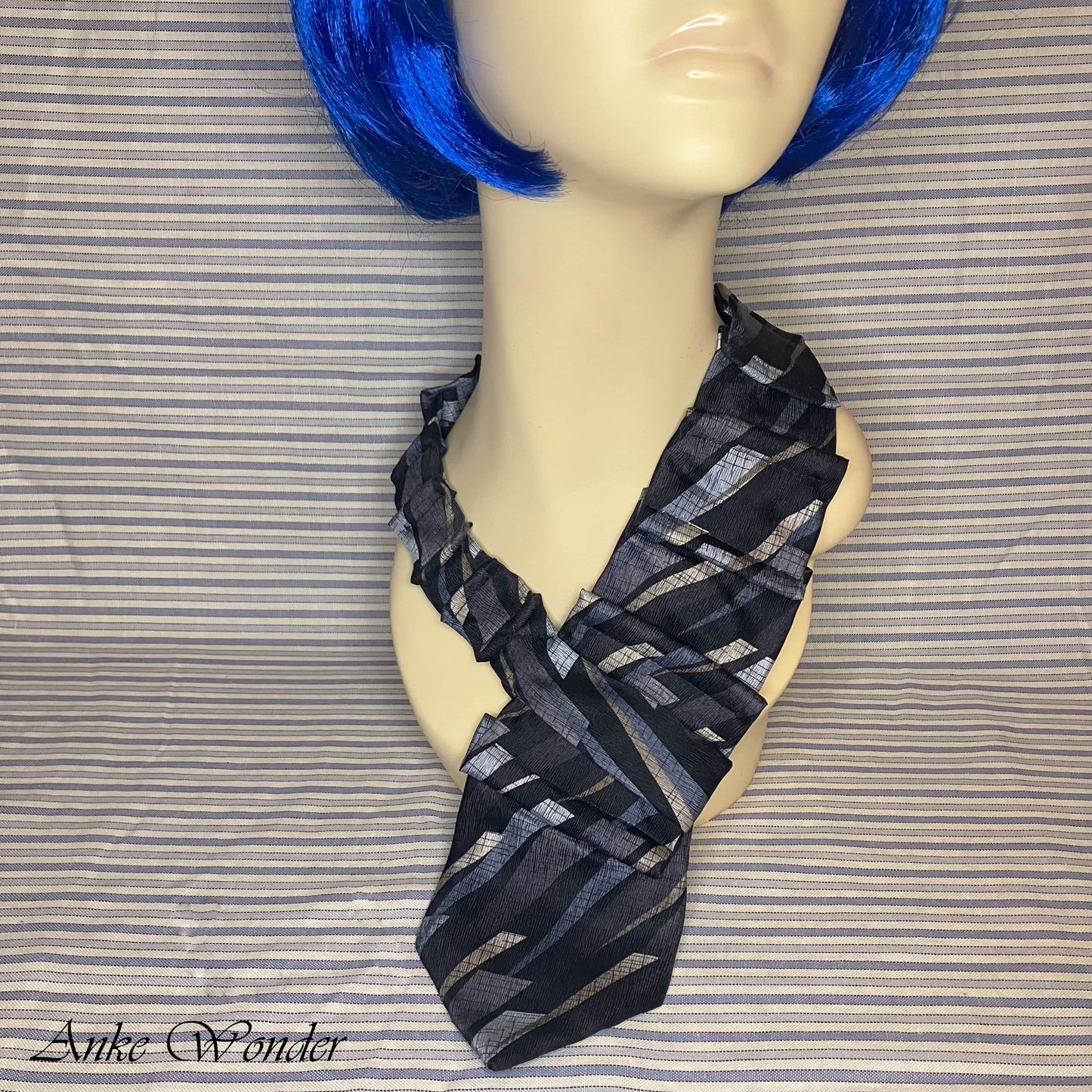 Closeup of the handmade blue and silver geometric silk necktie on a mannequin, showcasing the detailed hand-pleating.
