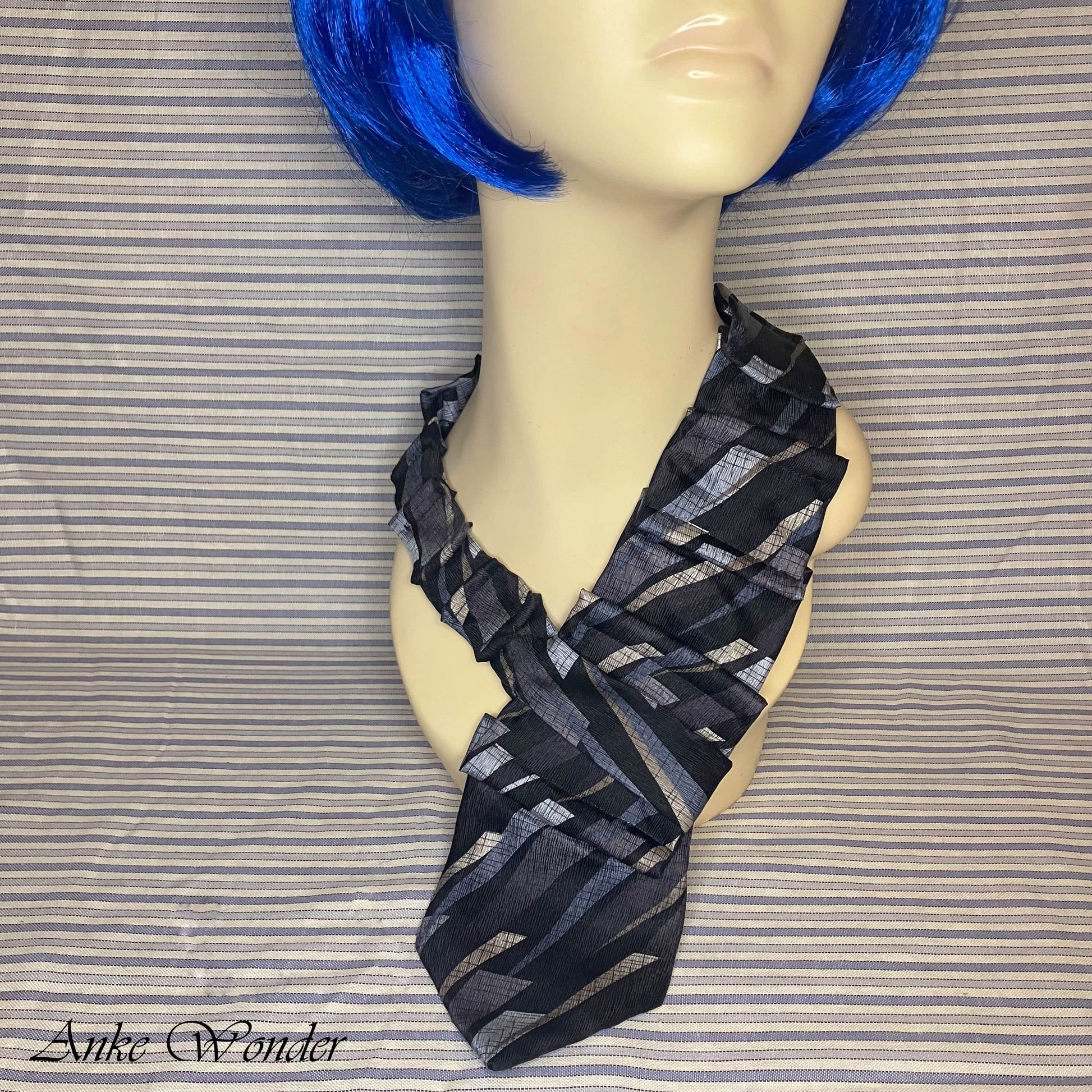Closeup of the handmade blue and silver geometric silk necktie on a mannequin, showcasing the detailed hand-pleating.