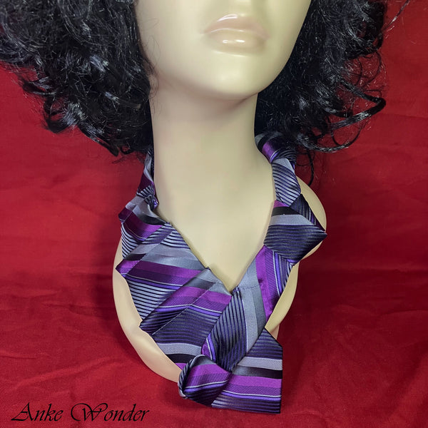 Close-up view of a purple silk necktie with geometric patterns and pyramid pleats on a mannequin, showcasing intricate craftsmanship from upcycled materials.