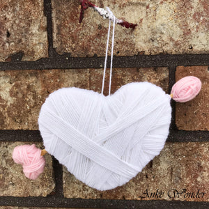 Handmade white Valentine's heart decoration with arrow, hanging in front of a brick wall.