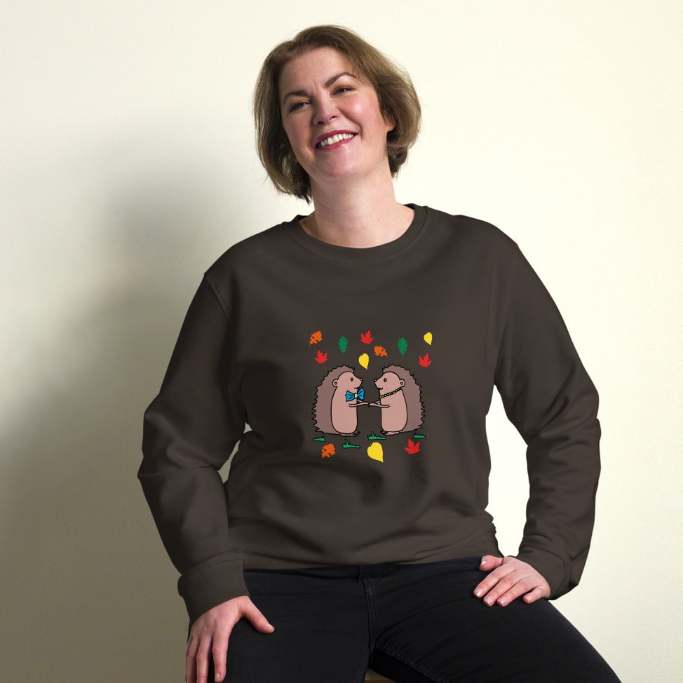 Plus-size model wearing Hedgehog Hugs Organic Cotton Women Sweatshirt in brown, featuring two hedgehogs holding hands surrounded by colorful leaves, designed by Anke Wonder.