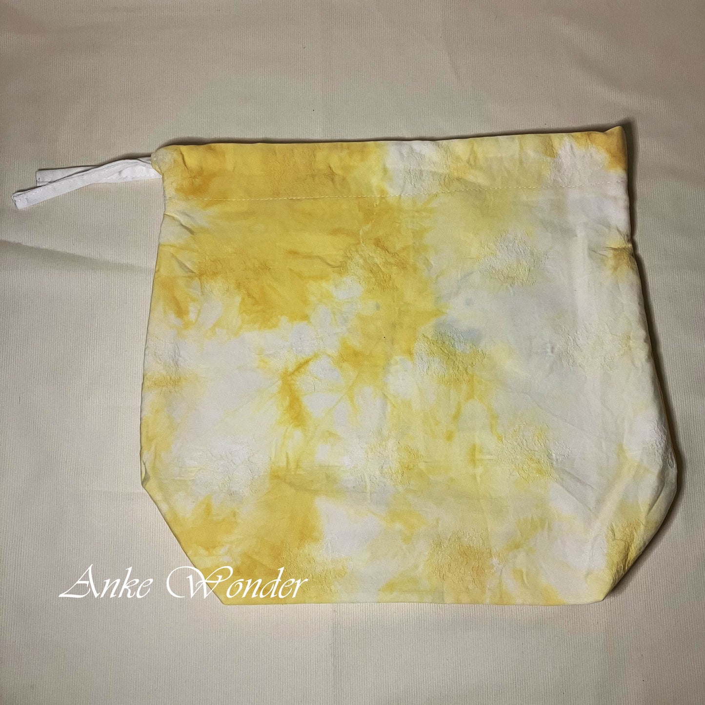Yellow and white tie-dye pouch on a beige background with 'Anke Wonder' branding.