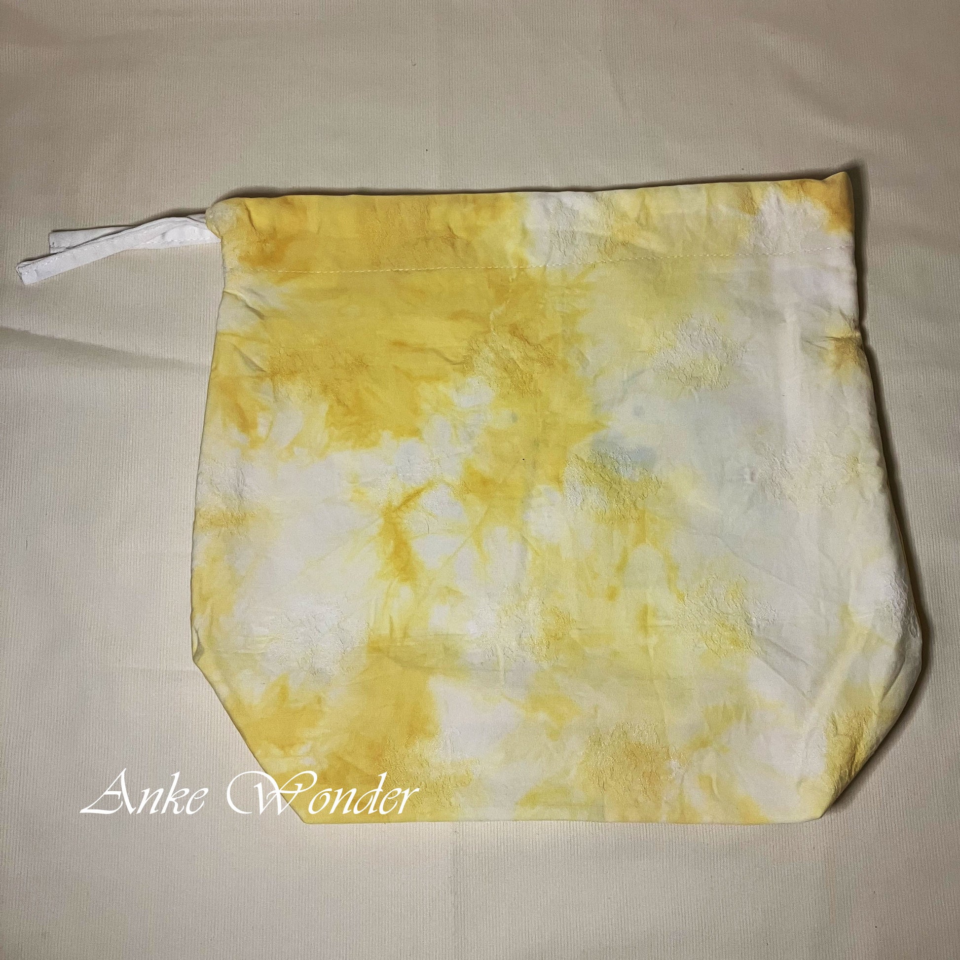 Yellow and white tie-dye pouch on a beige background with 'Anke Wonder' branding.