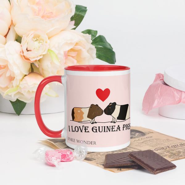 White ceramic mug with red rim, handle, and interior, featuring two guinea pigs nose-to-nose with a red heart above them and the text "I Love Guinea Pigs" by Anke Wonder.