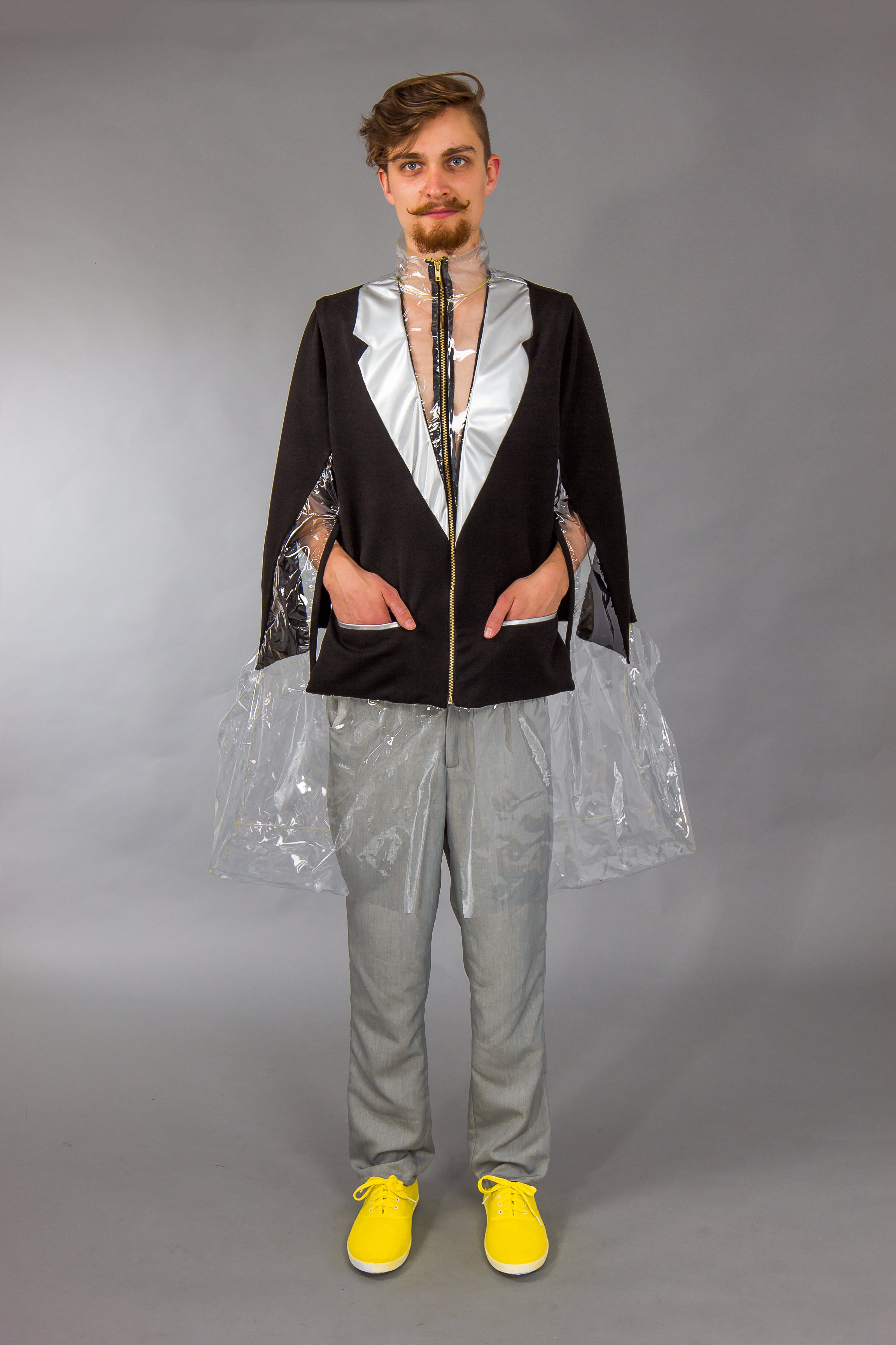Person wearing a black and silver jacket with a transparent plastic bag over it on a gray background