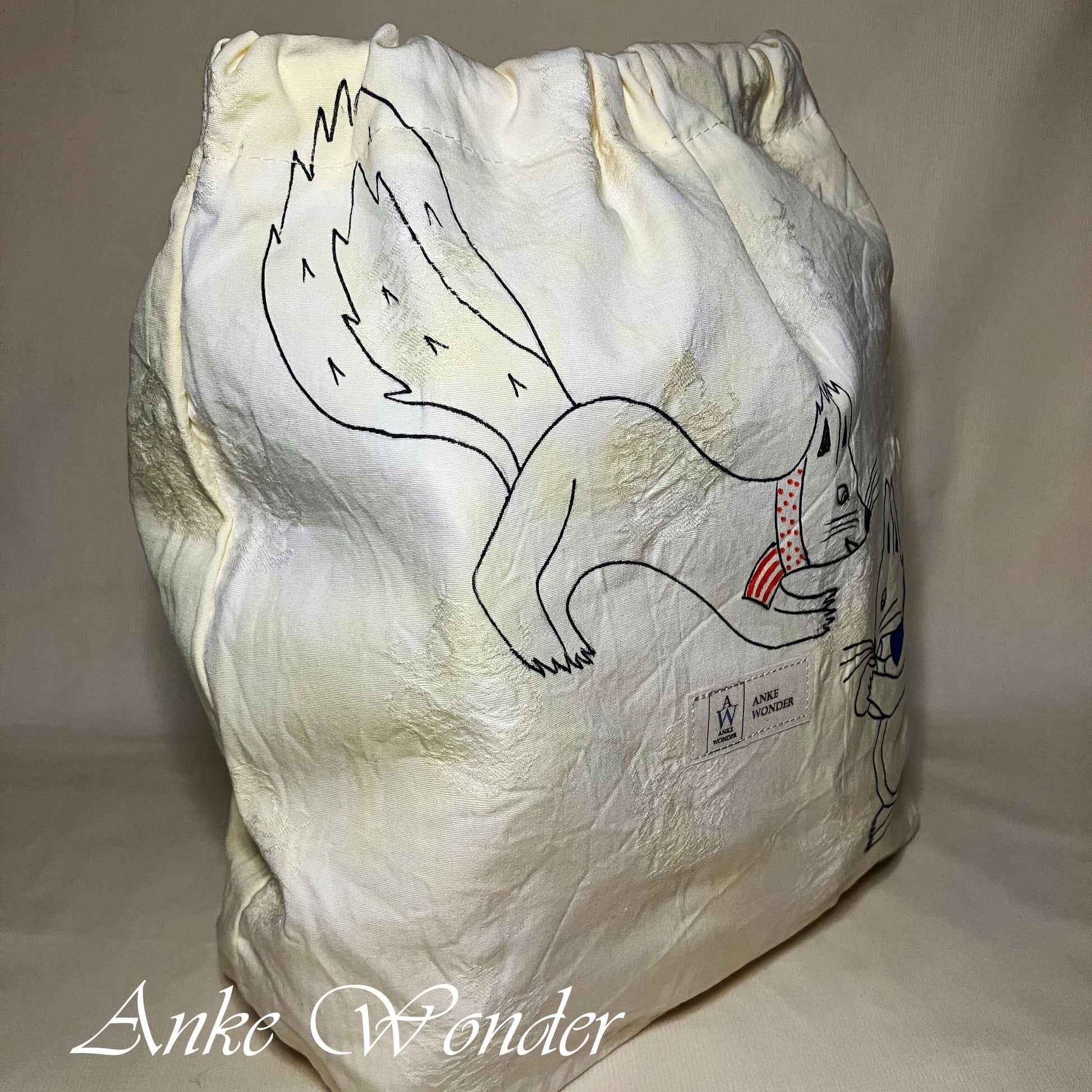 White drawstring bag with a black line drawing of two squirrels on a white background, featuring the brand 'Anke Wonder'.