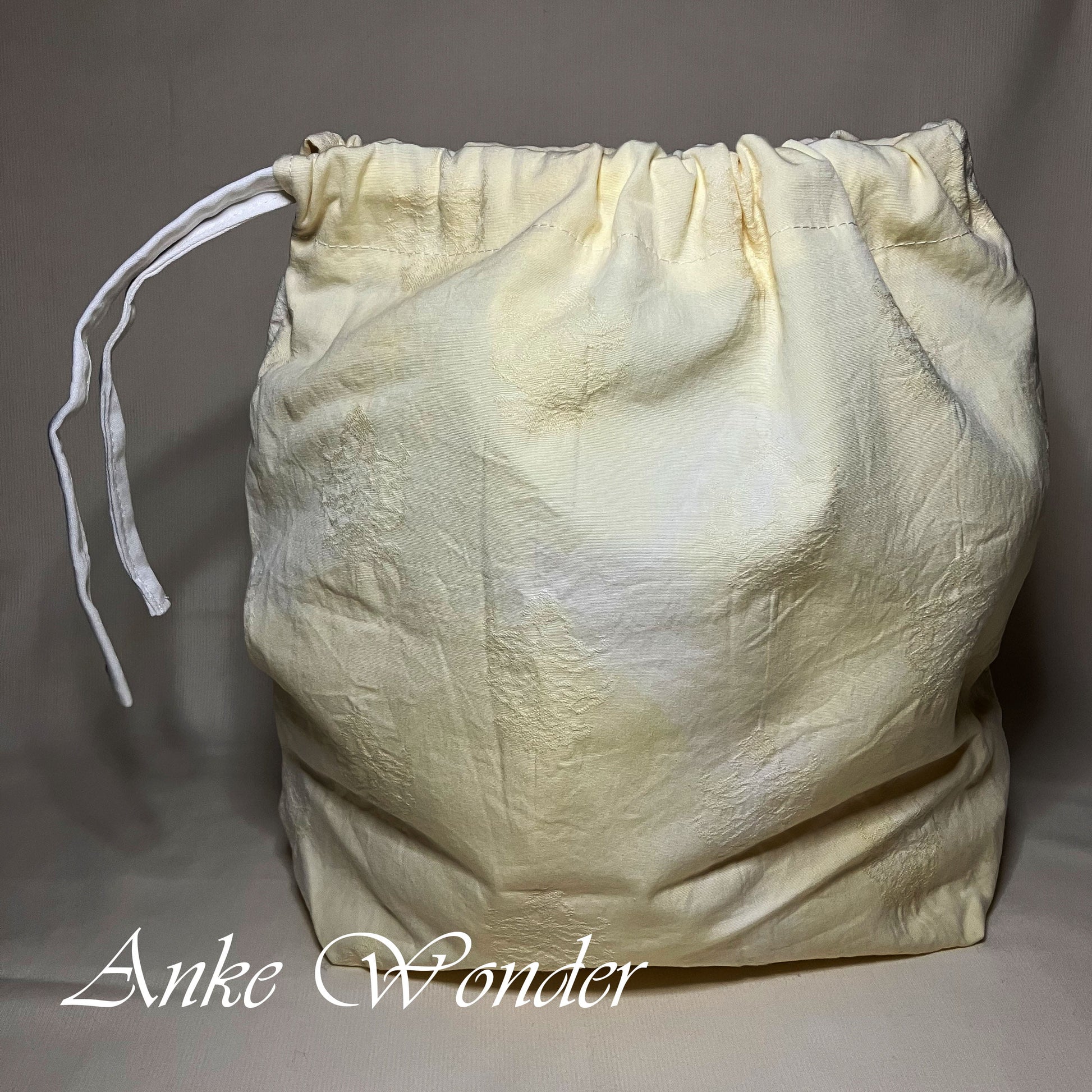White textured drawstring bag on a gray background with 'Anke Wonder' branding.