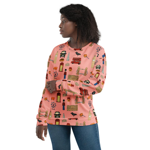 A black woman wears a cozy, long-sleeve sweatshirt with an all-over London-themed print on a soft pink background. The design features Big Ben, Tower Bridge, double-decker buses, black cabs, red phone booths, royal guards, and crows, creating a charming British aesthetic.