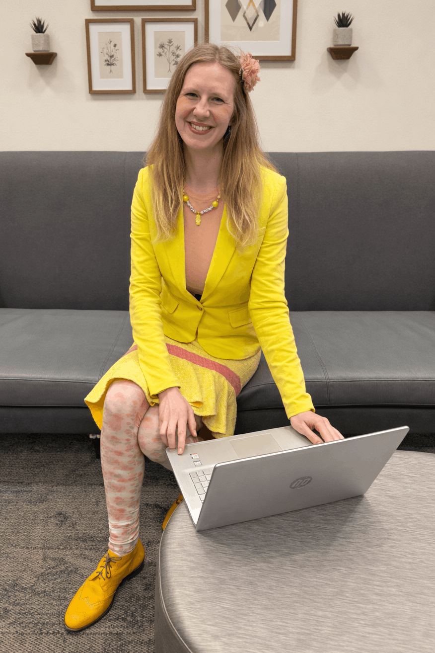 Anke Wonder in a yellow blazer sitting on a grey coach with a laptop in front of her.