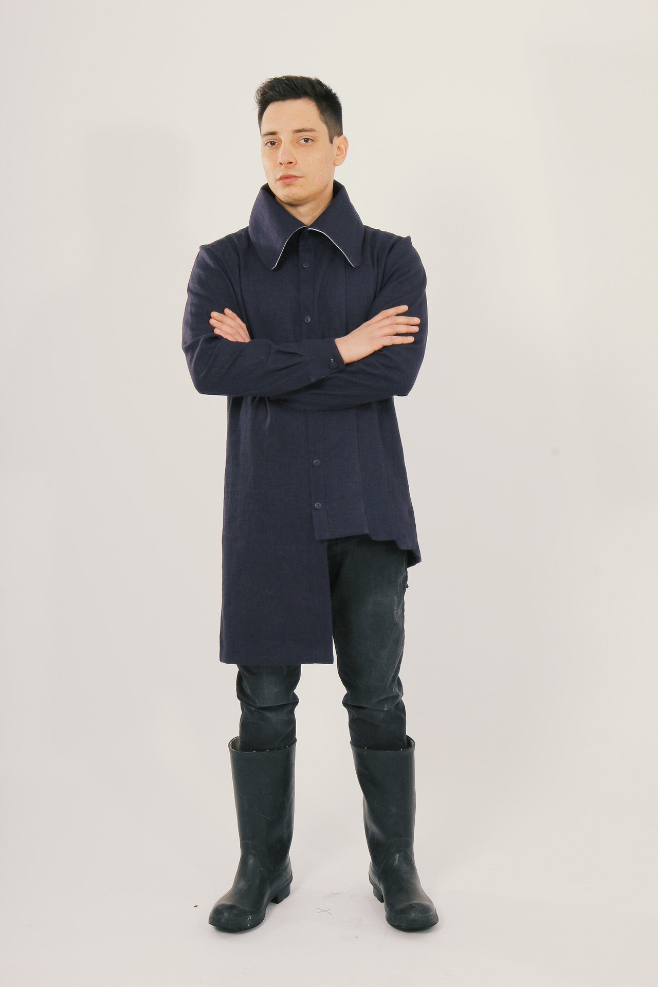 Man wearing a long navy shirt and black rain boots on a light gray background