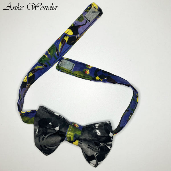 Black and white bird pattern organic cotton bow tie, laid flat on a table showing the adjustable Velcro closure.