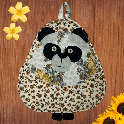 Front view of a panda-shaped potholder with a vintage floral pattern in warm tones, featuring black and white panda face details, button eyes, and a sweet embroidered smile. This charming kitchen accessory combines functionality with a retro-inspired design.