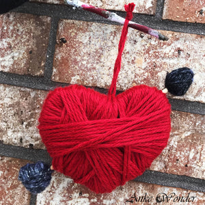 Handmade red Valentine's heart decoration with arrow hanging in front of a brick wall.