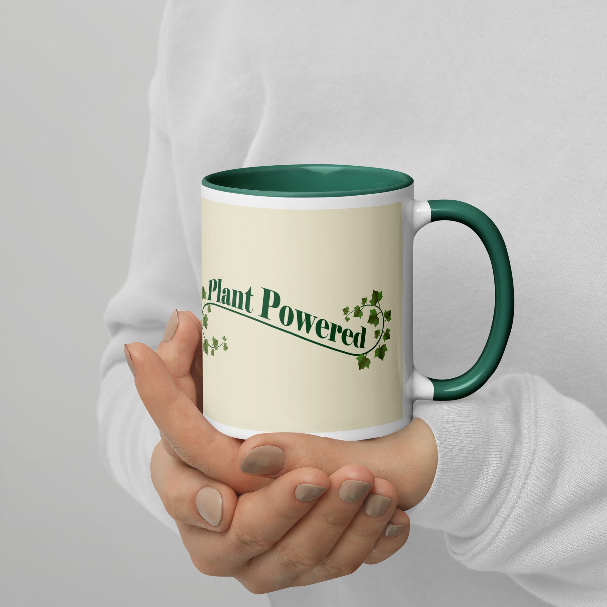 Right view of a ceramic mug with the phrase 'Plant Powered' in green, featuring a green handle and rim, held by a person wearing a white sweater.