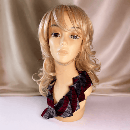 Mannequin head with a blonde wig and patterned tie against a beige curtain background